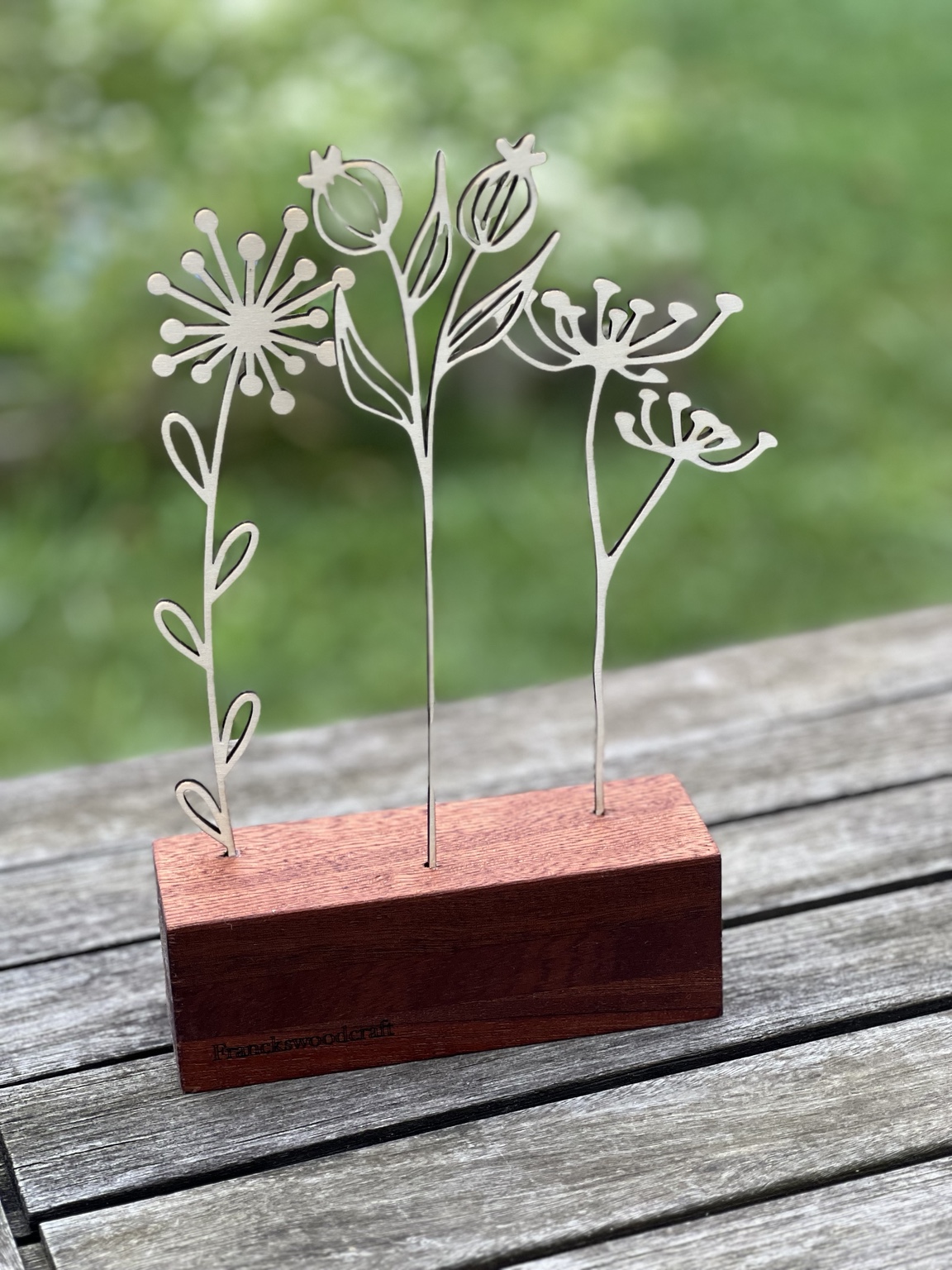Bouquet floral découpé au laser sur son socle en chêne, présenté à l’extérieur